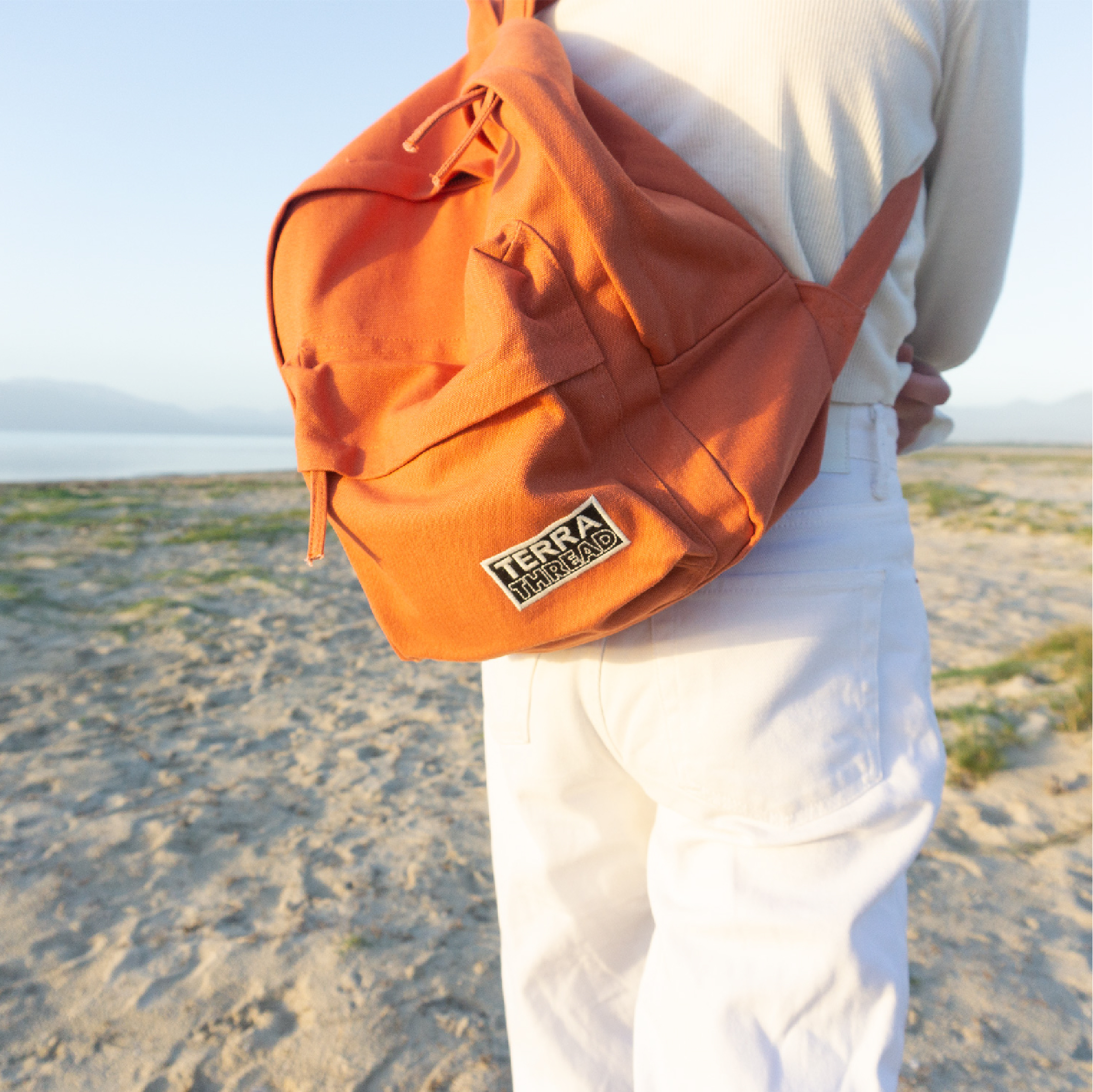 Person wearing all white with a bright orange Terra Thread book bag