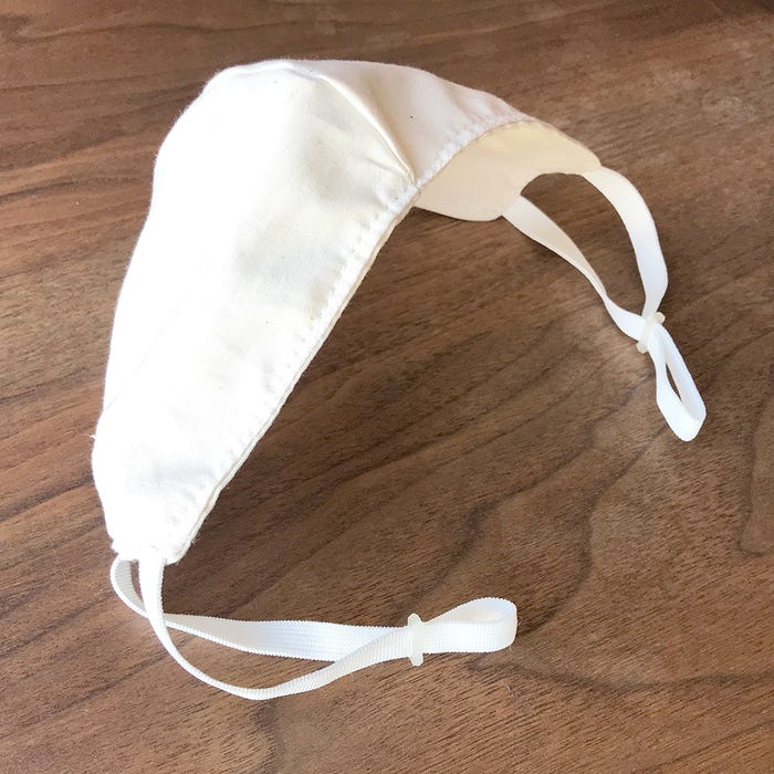 stiff, white mask with adjustable elastics sitting on top of a brown table.