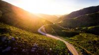 a road winding through the green California hills into the sunrise
