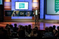 Matt Scott in a black suit giving a presentation to an audience at George Washington University's 2022 Planet Forward Summit