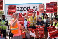 a group of Amazon workers striking. They are holding up red signs and yelling together.