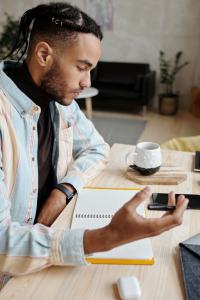 young black man wearing a flannel and studying or working at a desk with a notebook and a cup of coffee.