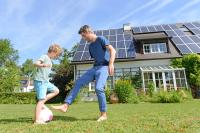 white dad and son playing soccer in the front yard of their house that is covered in solar panels