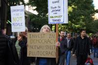 A people's march with signs that read "Invest in democracy, not wall street plutocracy" and "corporations are not people".
