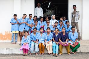 group of workers sitting in front of the Assisi Garment Factory