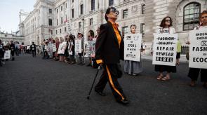 woman in black and yellow outfit walks in front of line of climate protestors from Extinction Rebellion