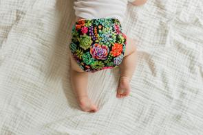 baby crawling on white bed sheets wearing a reusable diaper with a flower pattern
