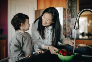 Asian mother and child washing strawberries in the kitchen