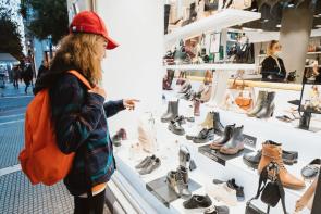 person wearing a red backpack and flannel window shopping for shoes