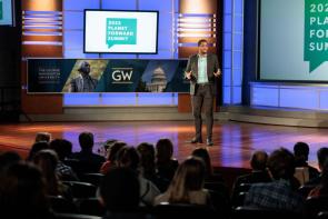 Matt Scott in a black suit giving a presentation to an audience at George Washington University's 2022 Planet Forward Summit