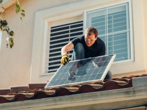 A man on a roof placing a solar panel. 