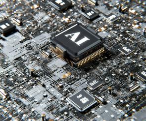 Close-up photograph of a black computer processor chip labeled 'AI' mounted on a circuit board, surrounded by various electronic components, gold pins, and circuitry