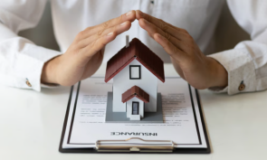 Hands over a miniature house sitting on an insurance policy