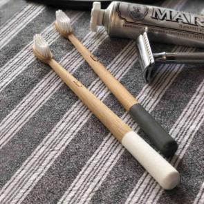 Truthbrush bamboo toothbrushes in white and gray colors next to safety razor and toothpaste tube on gray and white striped cloth.
