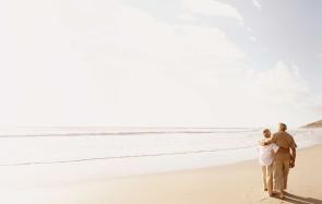 A retired couple walking arm-in-arm down the beach, people who can be helped by Sustainable Wealth Advisors