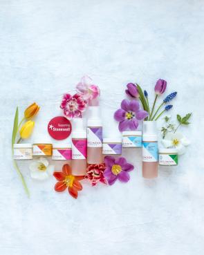 A line of colorful skincare products in bottles surrounded by colorful flowers