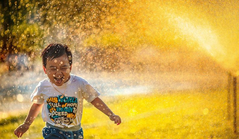 Image: child playing in water sprinkler. Title: 13 Ways to Save More than 65 Gallons of Water a Day