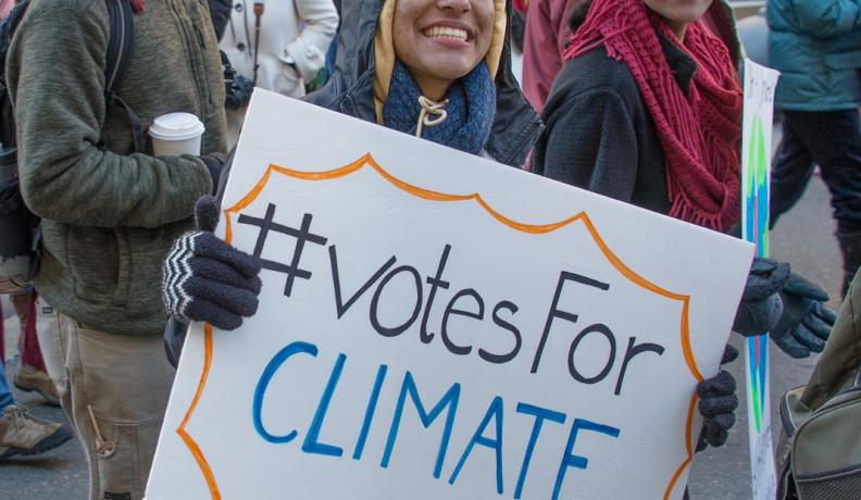 activist with sign that reads "hashtag Votes for Climate"