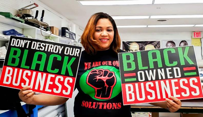 Keeanna Barber of WDB Marketing holds signs that say "Don't destroy our Black Business" and "Black Owned Business" that she printed at her shop.