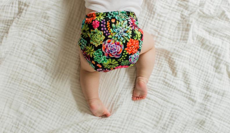 baby crawling on white bed sheets wearing a reusable diaper with a flower pattern