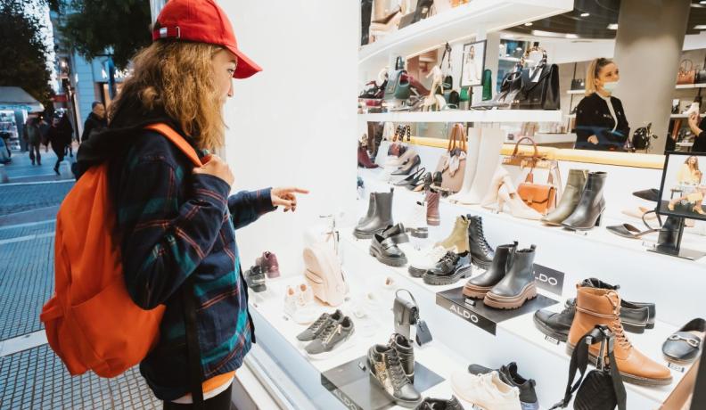 person wearing a red backpack and flannel window shopping for shoes
