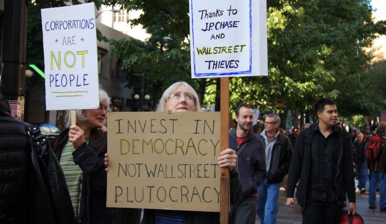 A people's march with signs that read "Invest in democracy, not wall street plutocracy" and "corporations are not people".