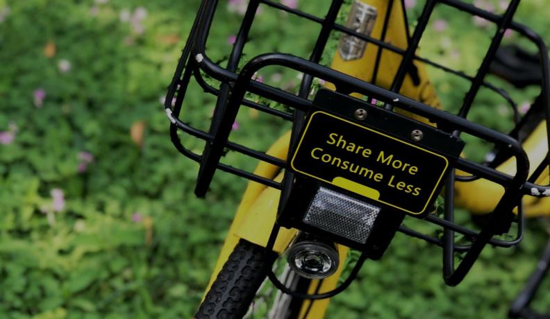 a yellow bike with a basket that reads "share more consume less"