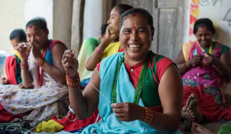 Nepali women dressed in colorful traditional attire making beaded bracelets. 