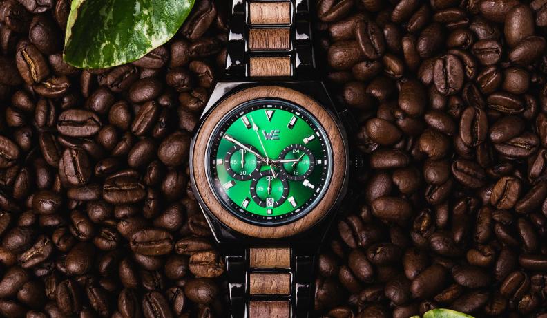 A watch made of walnut wood featuring a green face, the watch is set against a backdrop of coffee beans.