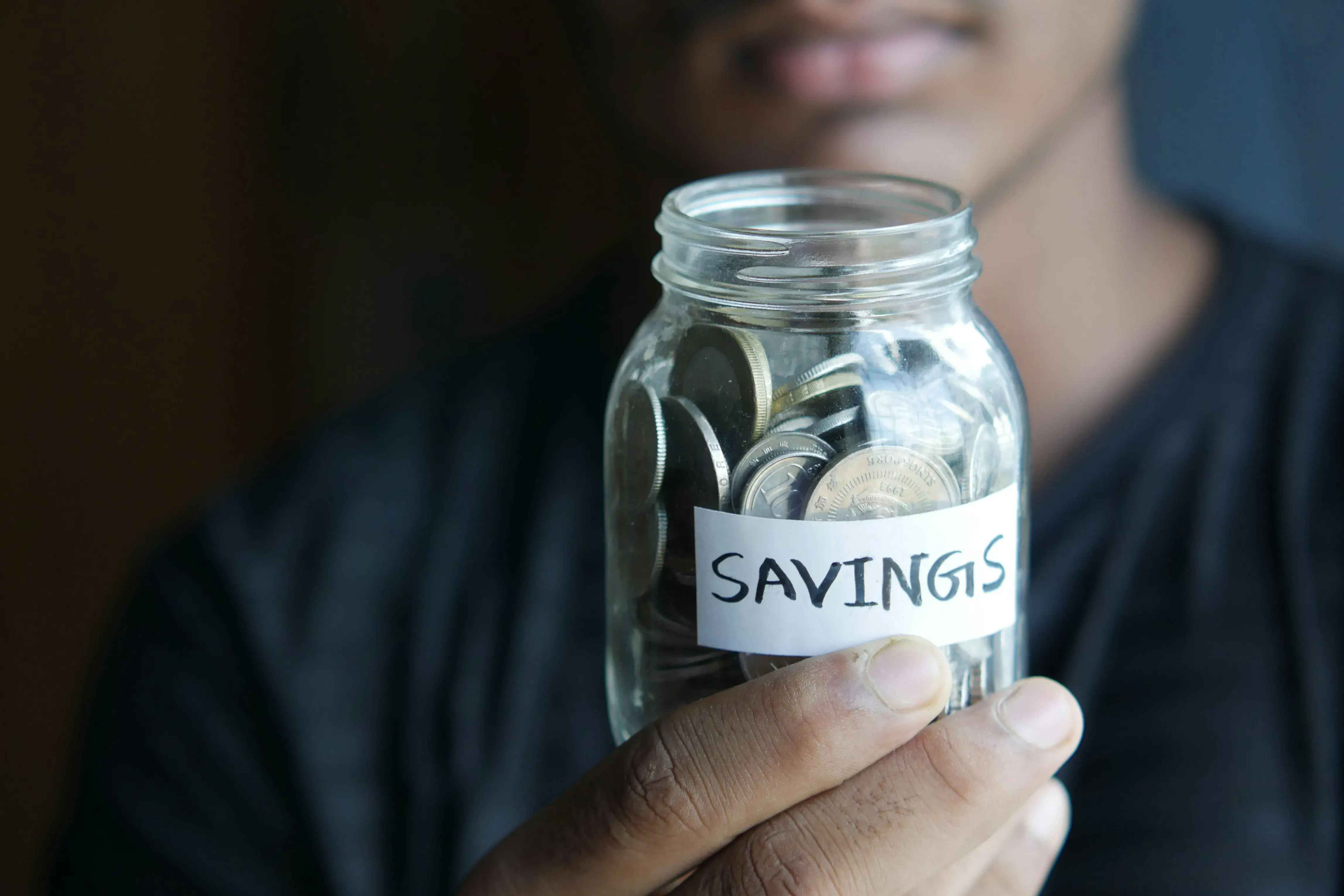 a man holding a jar of coins labeled "SAVINGS"