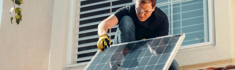 A man on a roof placing a solar panel. 