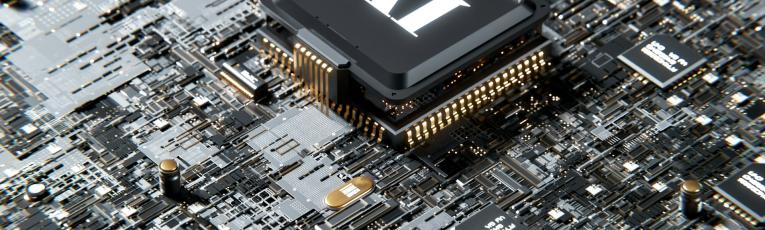 Close-up photograph of a black computer processor chip labeled 'AI' mounted on a circuit board, surrounded by various electronic components, gold pins, and circuitry