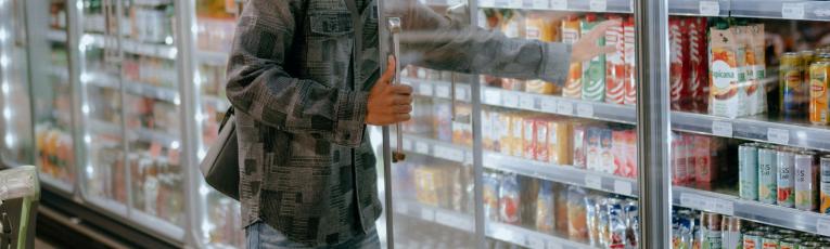 A young man shopping in the refrigerated aisle of a supermarket. 