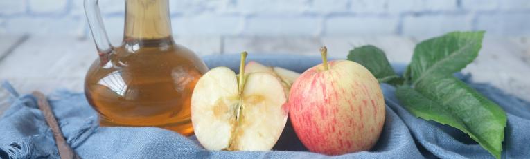 bottle of vinegar next to two apples. One of the apples is sliced in half to see the inside.