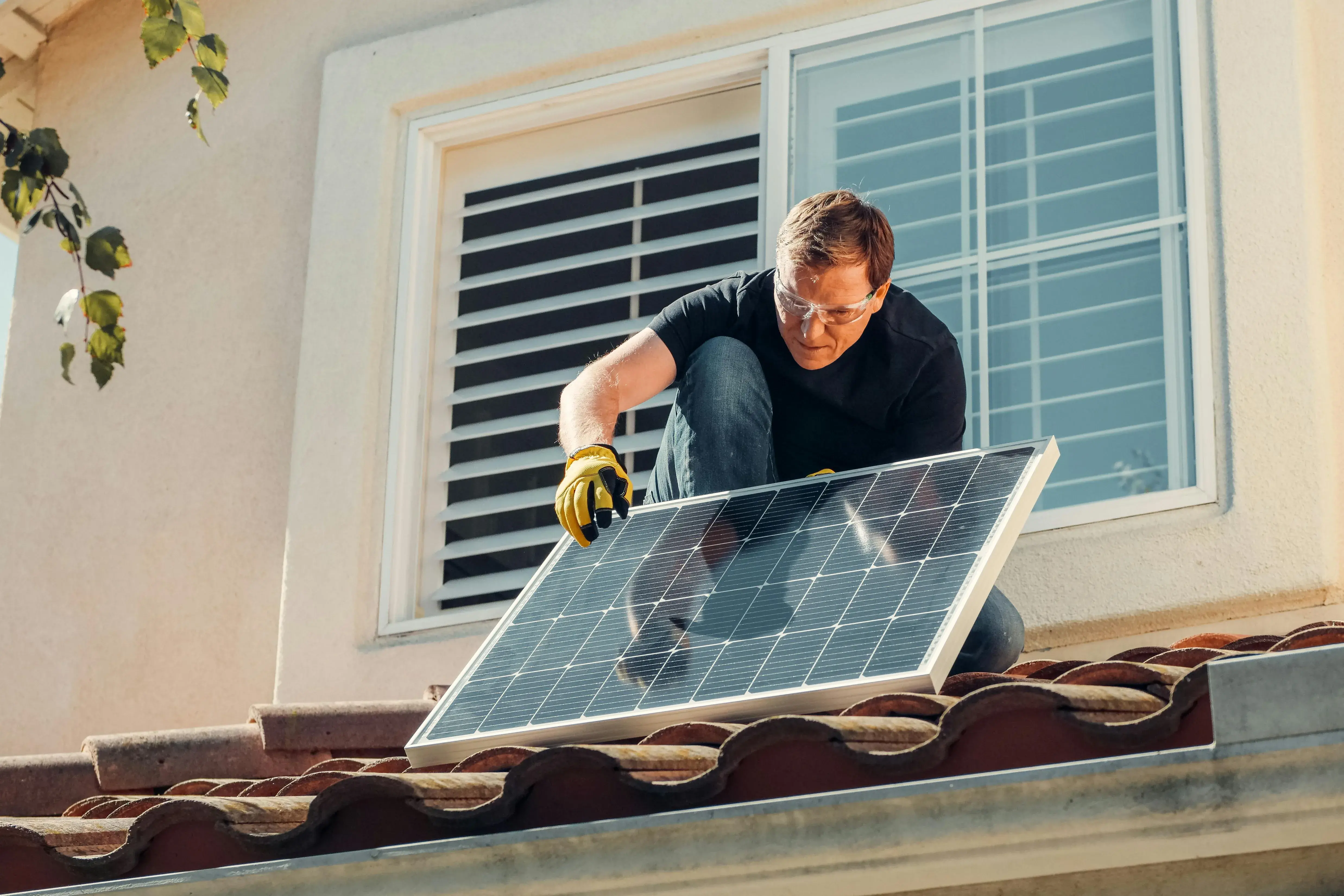 A man on a roof placing a solar panel. 