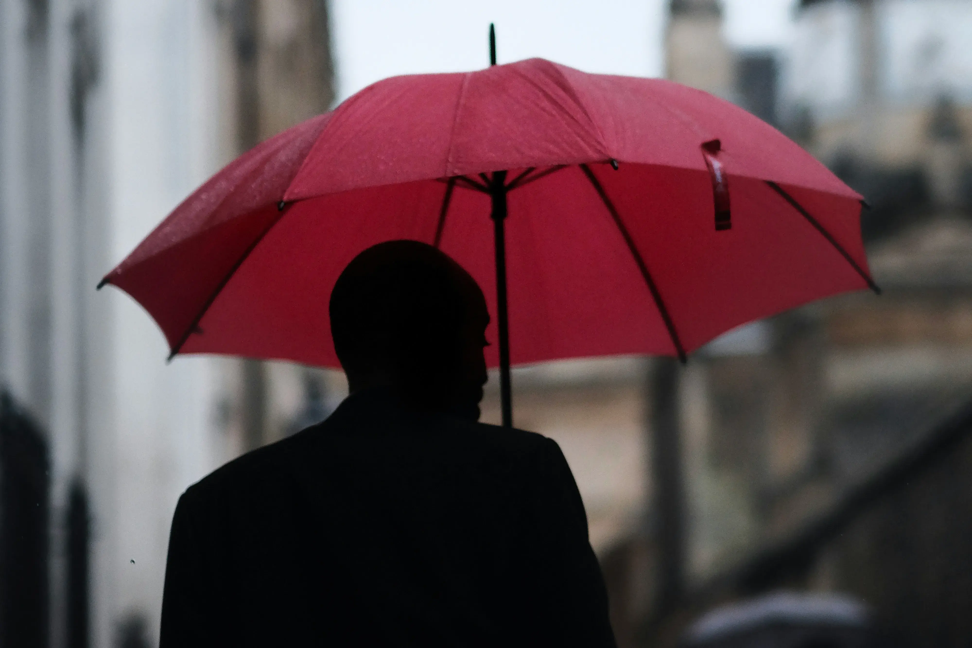 a man with a red umbrella disappears down senate house passage in cambridge uk