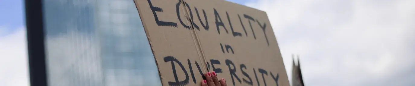 A hand holding a cardboard sign reading: "Equality in Diversity"