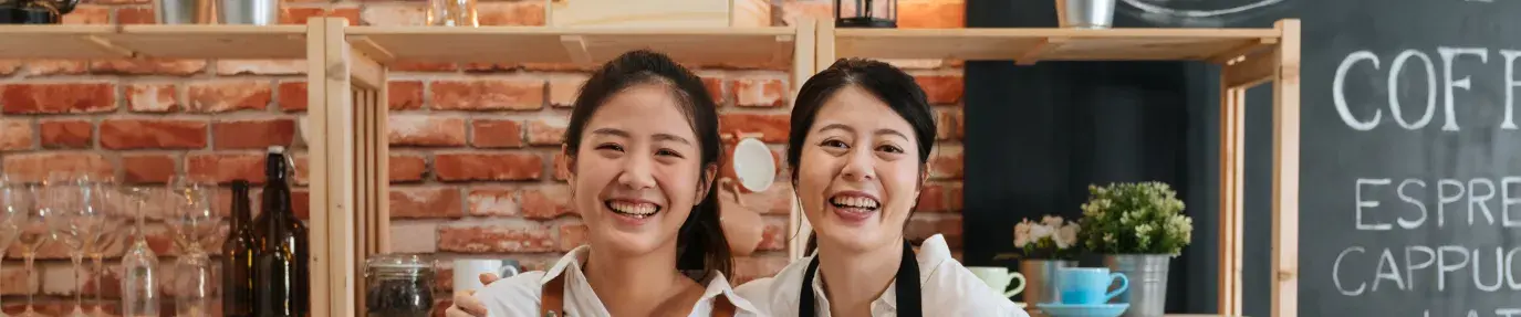 mother and daughter wearing aprons and smiling. They are coffee shop owners ready to make coffee.