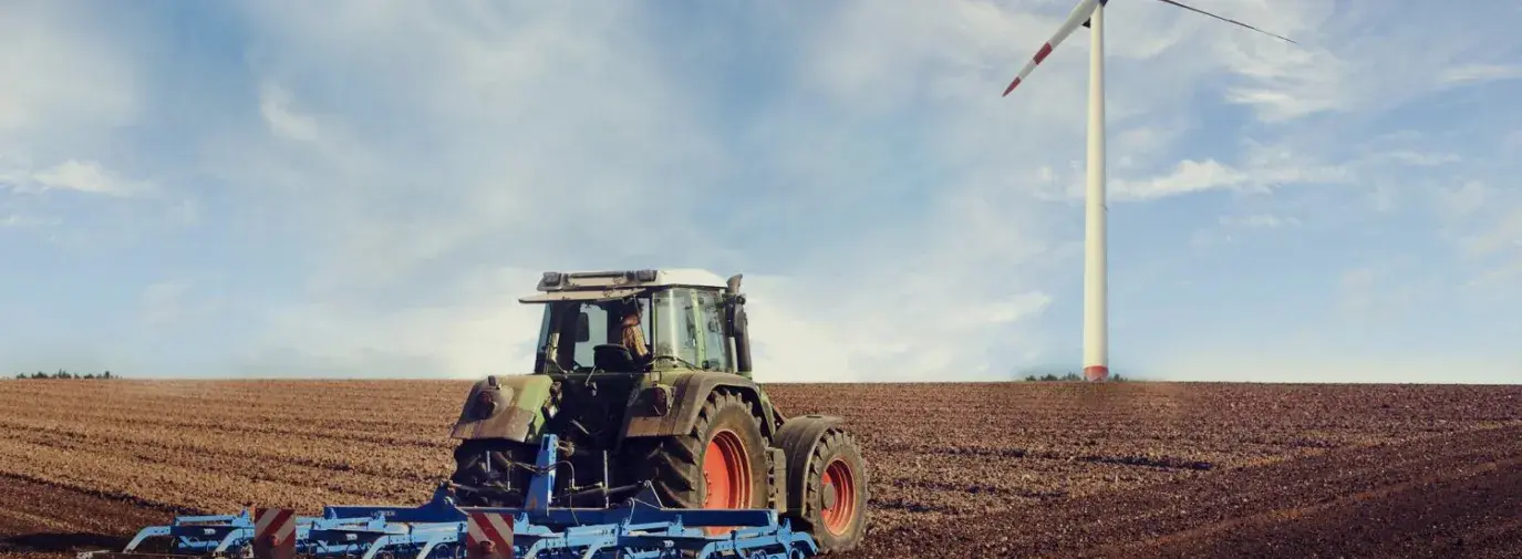 Image: tractor on a field with a wind turbine. Topic: Regenerative Agriculture.