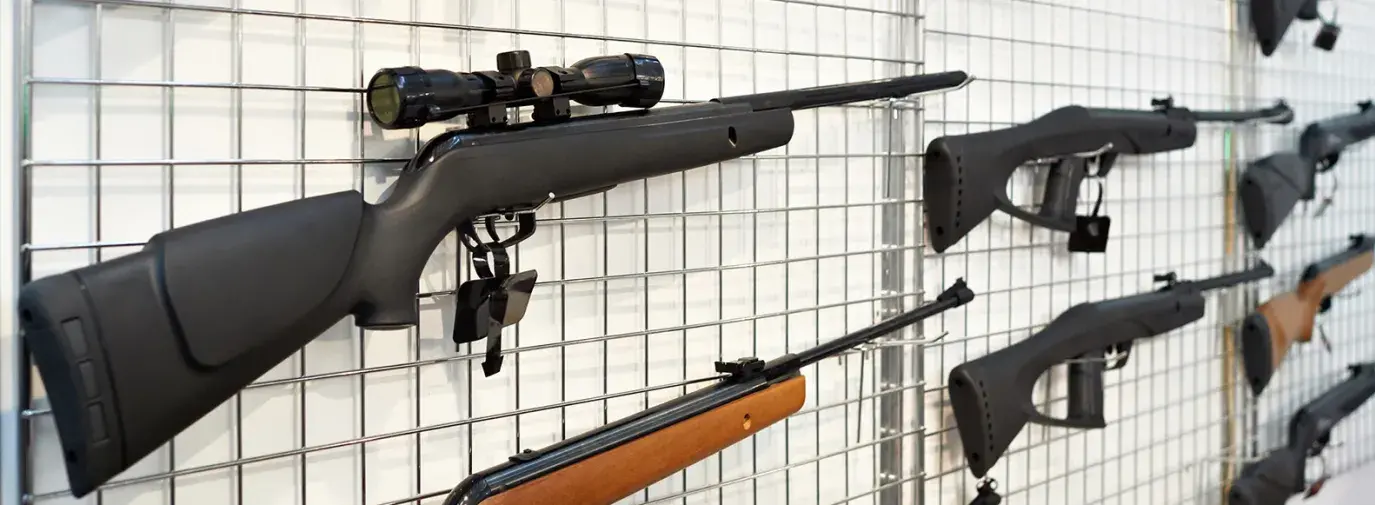 Image: guns on a rack. Title: Are You Unintentionally Investing in Gun Manufacturers?