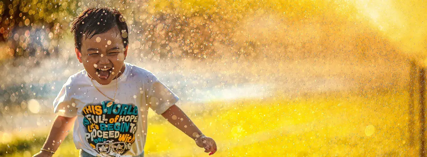 Image: child playing in water sprinkler. Title: 13 Ways to Save More than 65 Gallons of Water a Day