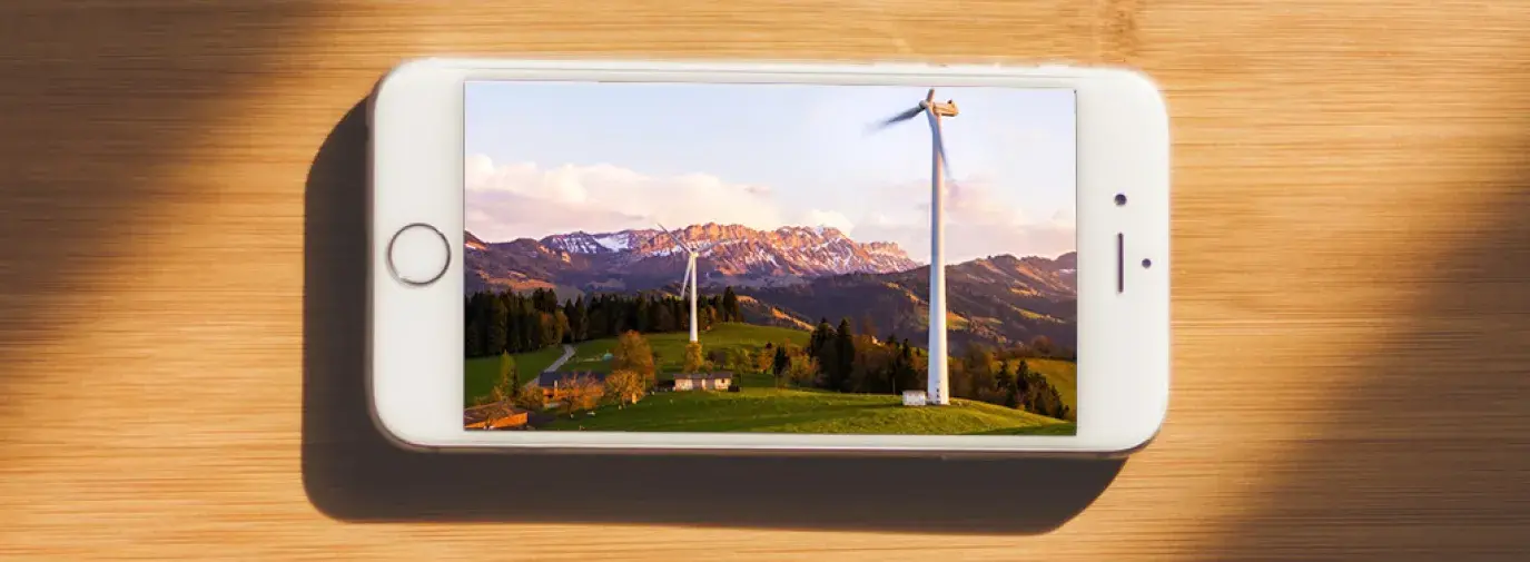Image: cell phone on table with photo of wind turbines in mountainous region. Title: Verizon Flunks Green America's Scorecard Grading Wireless Companies on Clean Energy