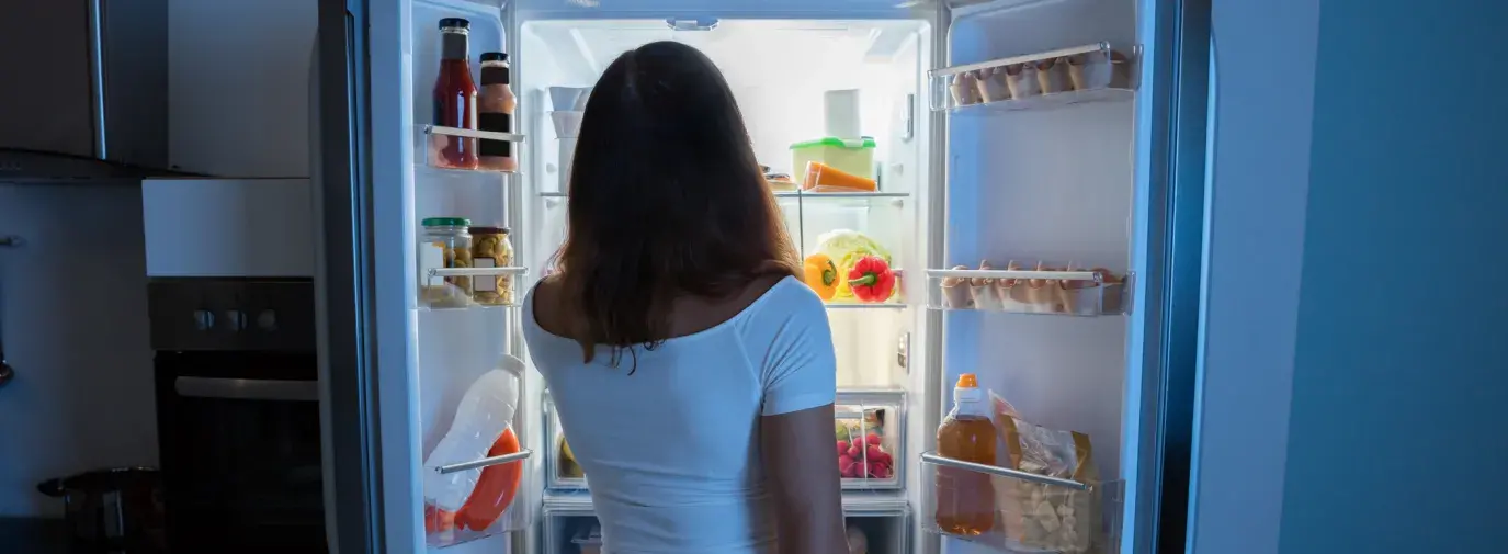 Image: woman looking in fridge at night. Topic: 5 Ways to Fight Food Waste