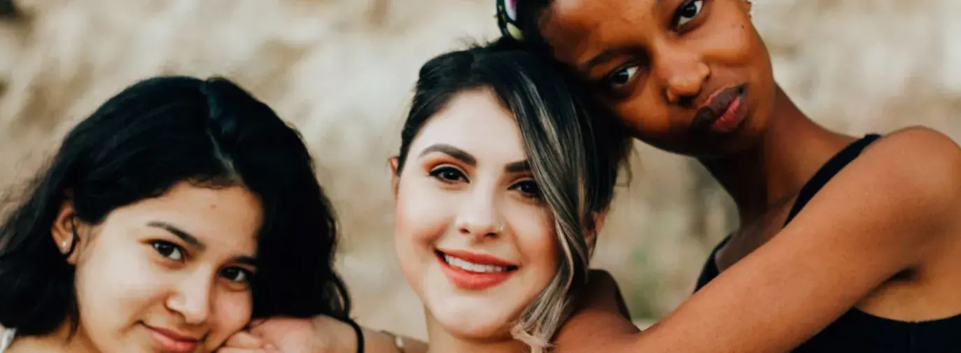 Portraiture of three diverse women leaning on each other's shoulders. The one in the middle is throwing up a peace sign. Women-owned green business is booming.