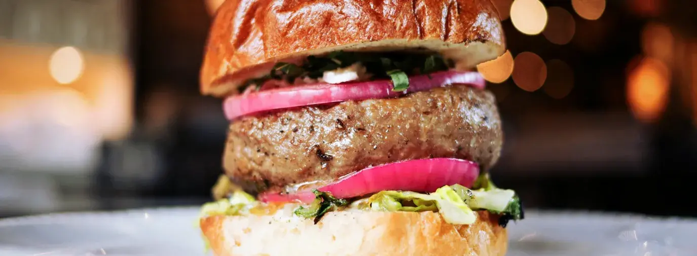 burger with lettuce, red onion, and tomato on a toasted bun with bokeh lights in the background