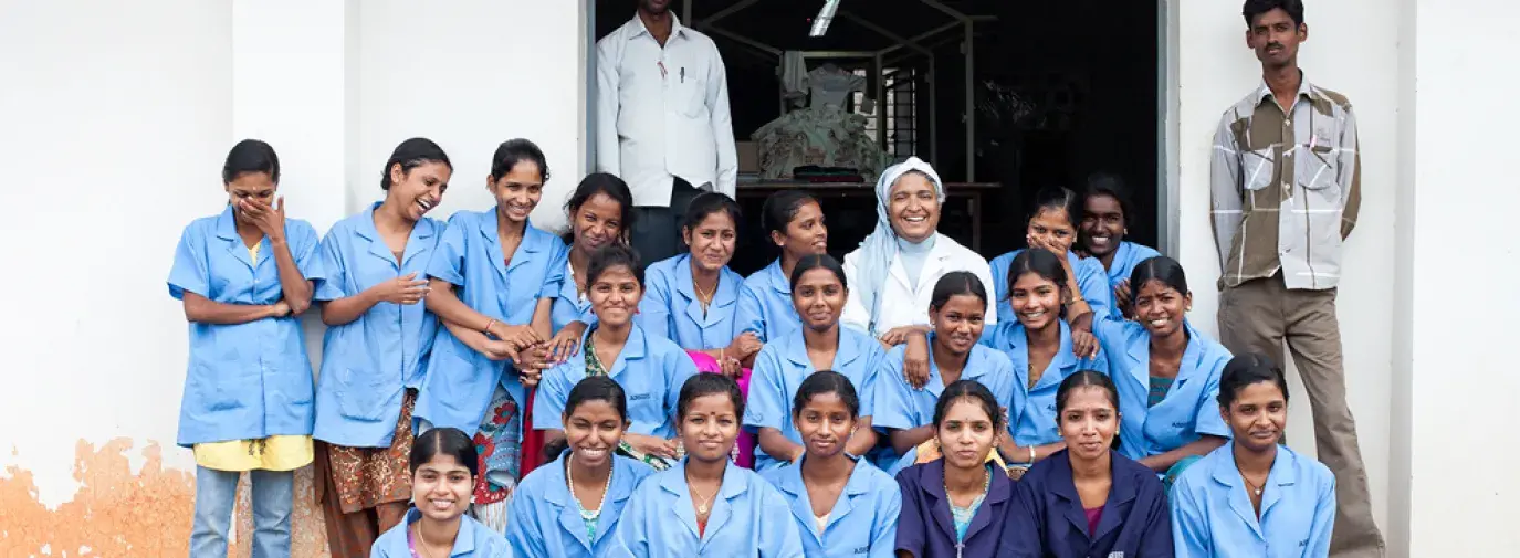 group of workers sitting in front of the Assisi Garment Factory