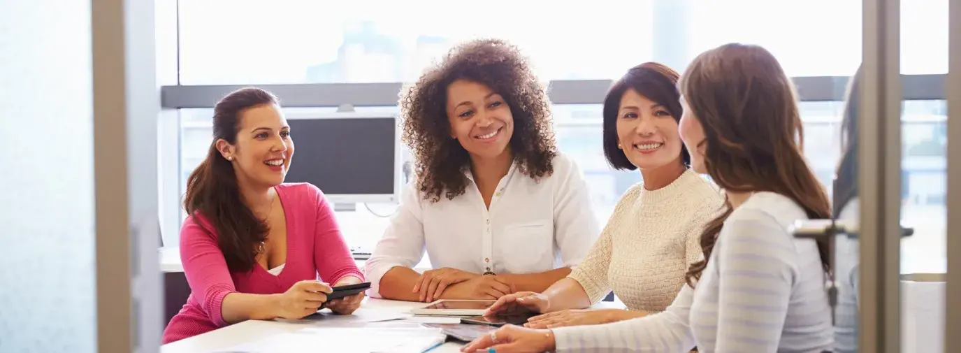 four women sitting around a desk in an office, gender lens investing benefits