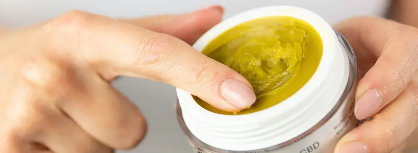 white person rubs their index finger in a yellow balm labeled "Therapeutic CBD skin balm", hemp-cbd is on the rise