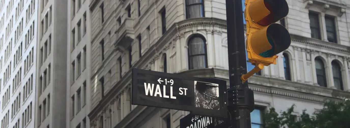 black street pole with street light and street sign saying "Wall St" against the backdrop of a tall, grey building with lots of windows, socially responsible investing must be a requirement