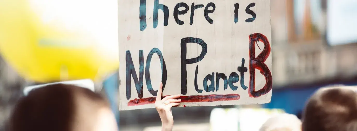 Image: protestor holding sign that says "There is no Planet B." Title: What Do Corporate Commitments for Climate Week Really Mean?